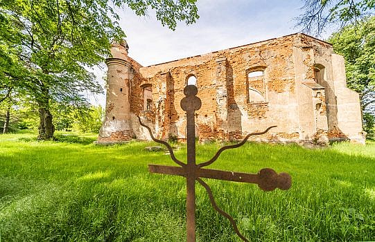 Metalowy krzyż na pierwszym planie, w tle ruiny kościoła w Chojnicy