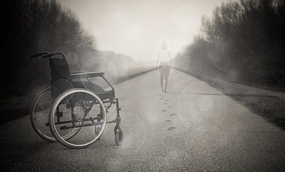 Wózek inwalidzki na drodze, w tle odchodząca kobieta
