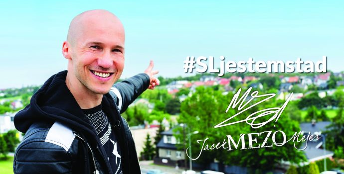 Piosenkarz Jacek Mezo Mejer na tle Suchego Las. Na zdjęciu napisy #SLkestemstad oraz podpis artysty