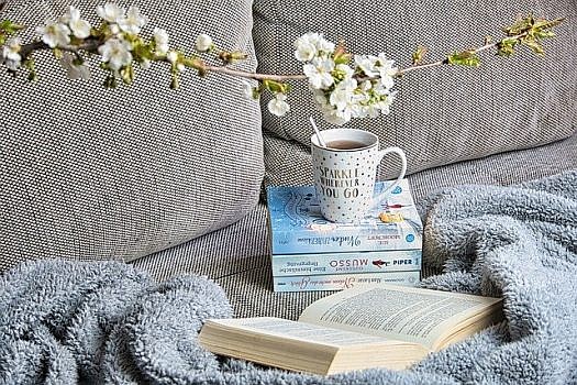 Kanapa, na której leżą koc, książki i kubek