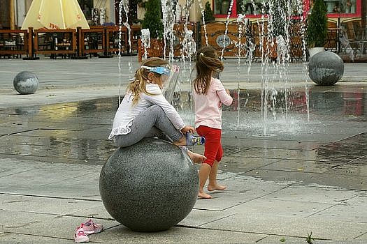 dzieci bawiące się na placu z fontannami
