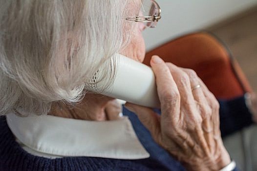 Zbliżenie na twarz starszej kobiety - prawy profil. Kobieta przy uchu trzyma słuchawkę od telefonu.