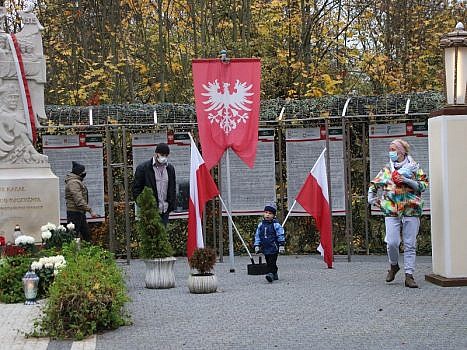 Panteon Powstania Wielkopolskiego w Biedrusku. W tle flaga powstańcza i flagi Polski. Wśród nich rodzina z dziećmi.