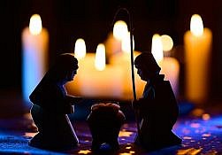 Jezus i Maryja klękający przy żłobku. W tle palące się świece.