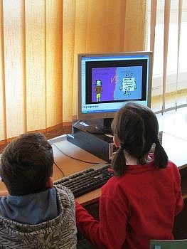 Dzieci siedzące przy stole przed komputerem.