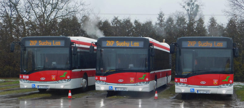 Trzy biało-czerwone autobusu miejskie stoją obok siebie na betonowym placu