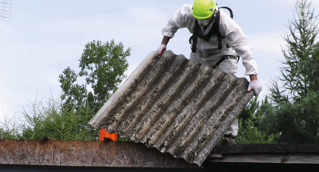 Mężczyzna na dachu ściągający płytę azbestu