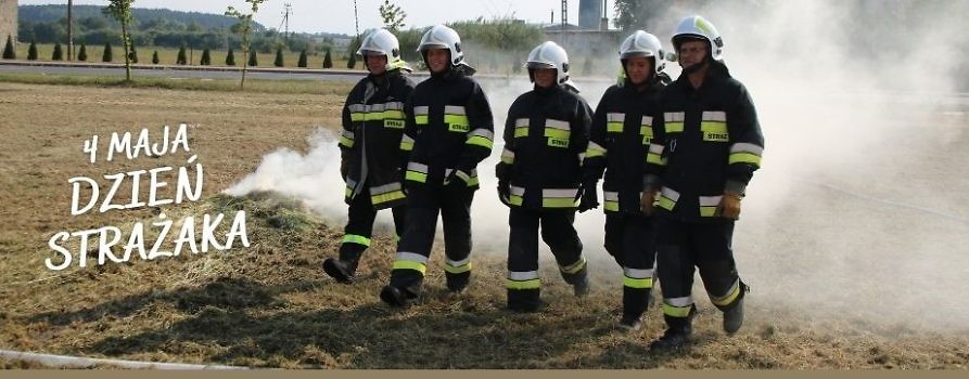 pięciu strażaków idzie po łące, za nimi jest dym z podpalonej trawy, napis 4 maja dzień strazaka