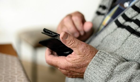 Zbliżenie na ręce osoby starszej trzymającej telefon.
