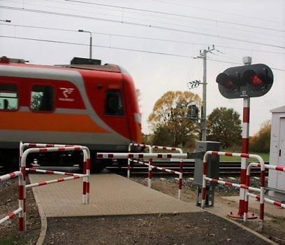 Pociąg jadący obok przejazdu kolejowego z zamkniętymi rogatkami.