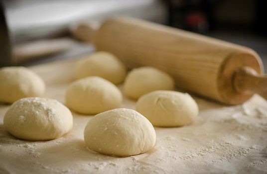 Ciasto w formie bułek wraz z wałkiem leżące na stolnicy.