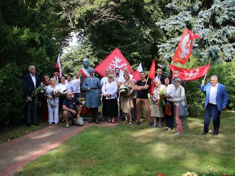 Zdjęcie przy pomniku Romana Dmowskiego w Chludowie z uczestnikami uroczystości, którzy trzymają flagi.