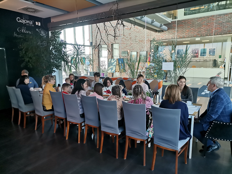 Grupa 15 osób przy stole w restauracji. W tle hol Centrum Kultury w Suchym Lesie.