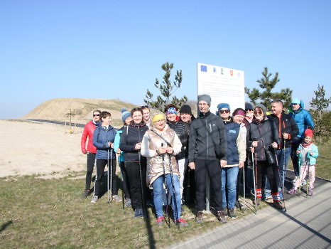 Grupa z kijkami do nordic walking przy tablicy z informacją o unijnym projekcie.