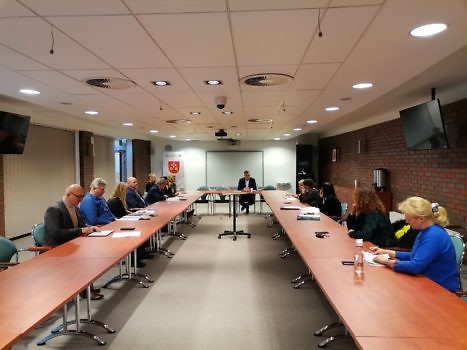 Kilkanaście osób przy stole ustawionym w U, na sali konferencyjnej.