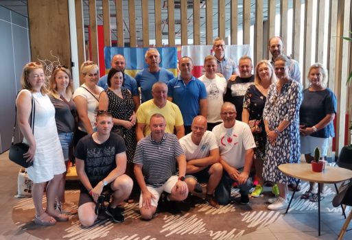Grupa kilkunastu osób z gmin partnerskich pozujących do zdjęcia. W holu hotelowym w tle flagi polska i ukraińska.