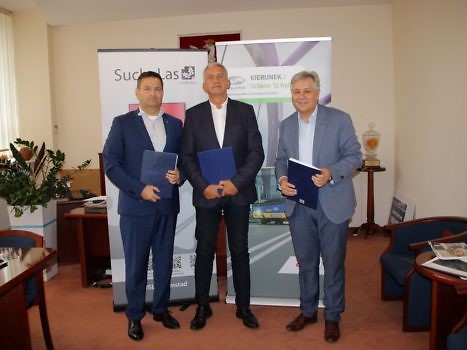 Wójt Gminy w obecności Prezesa ZKP i Dyrektora Sprzedaży firmy Solaris stoją na tle rollupaów