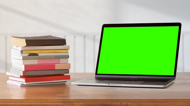 Laptop i książki położone na stole.