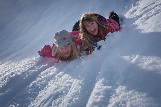 Dzieci zjeżdżające na brzuchu po śniegu.