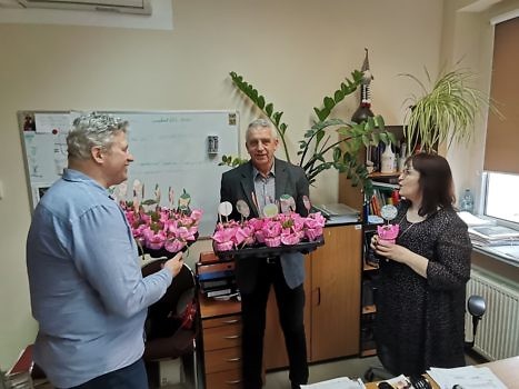 Na zdjęciu dwóch panów w biurze wręczających kwiaty pani.