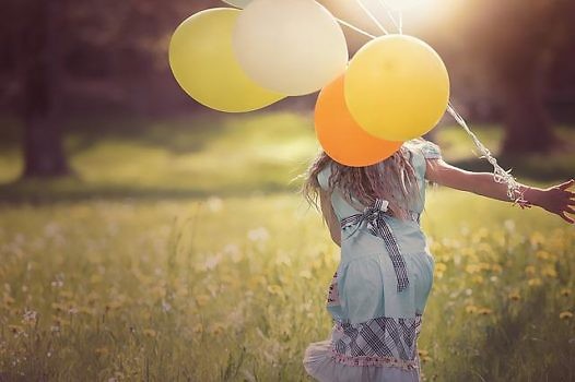 Dziewczynka z balonami w ręku biegnąca po łące.