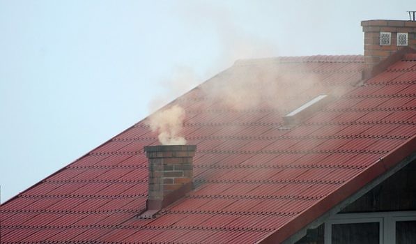 Widok na kawałek dachu z kominem, z którego wylatuje dym.