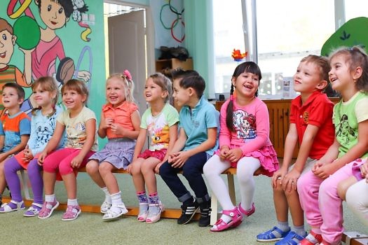 Dzieci siedzące na ławeczce w przedszkolu.