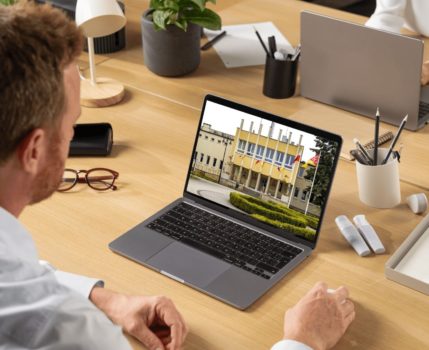 Biurko z laptopami, przy którym siedzą dwie osoby. Na jednym z laptopów zdjęcie frontu urzędu gminy w suchym Lesie.