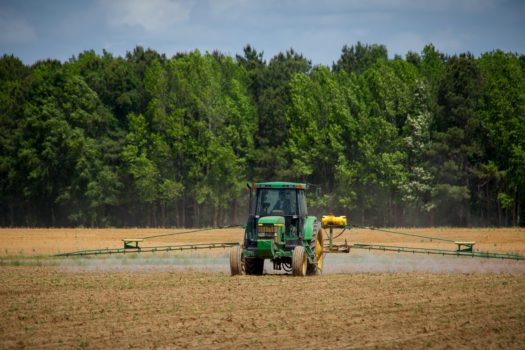 Traktor jadący po polu i wykonujący opryski.