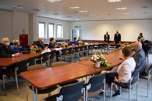 Widok na salę, w której przy owalnym stole siedzą jubilaci, w oddali przemawia Wójt