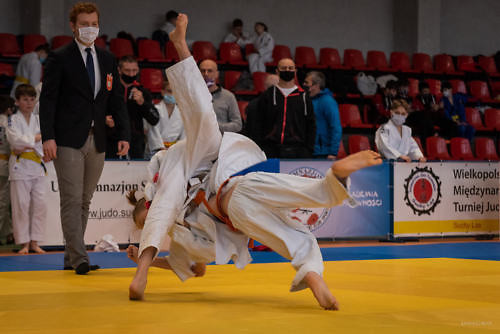 Zawodnicy judo podczas walki, moment rzutu na matę, w tle sędzia