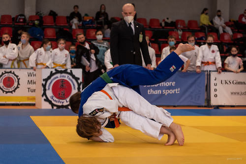 Zawodnicy judo podczas walki - jeden w granatowym stroju, drugi w białym, moment rzutu na matę, w tle sędzia