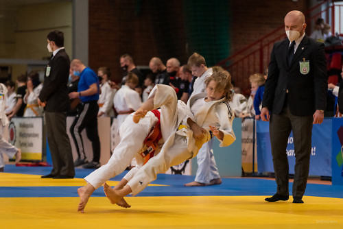 Dwóch zawodników walczy w judo, moment położenia, sędzia przygląda się walce. 