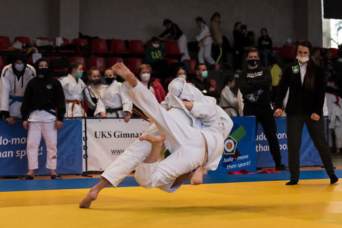Zawodnicy judo podczas walki, moment rzutu na matę, w tle sędzia